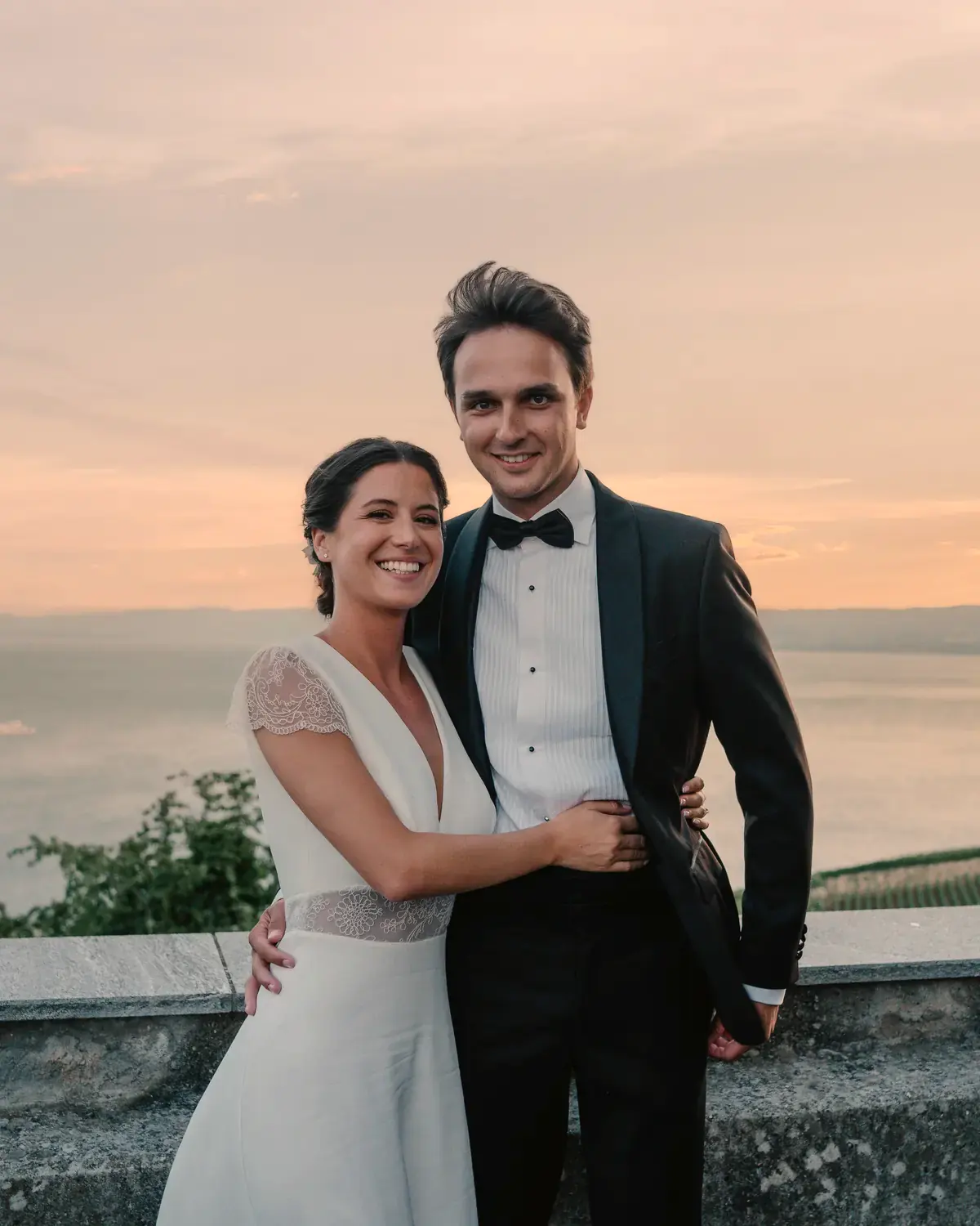 Un couple enlacé sur une terrasse au coucher du soleil, le lac en contrebas