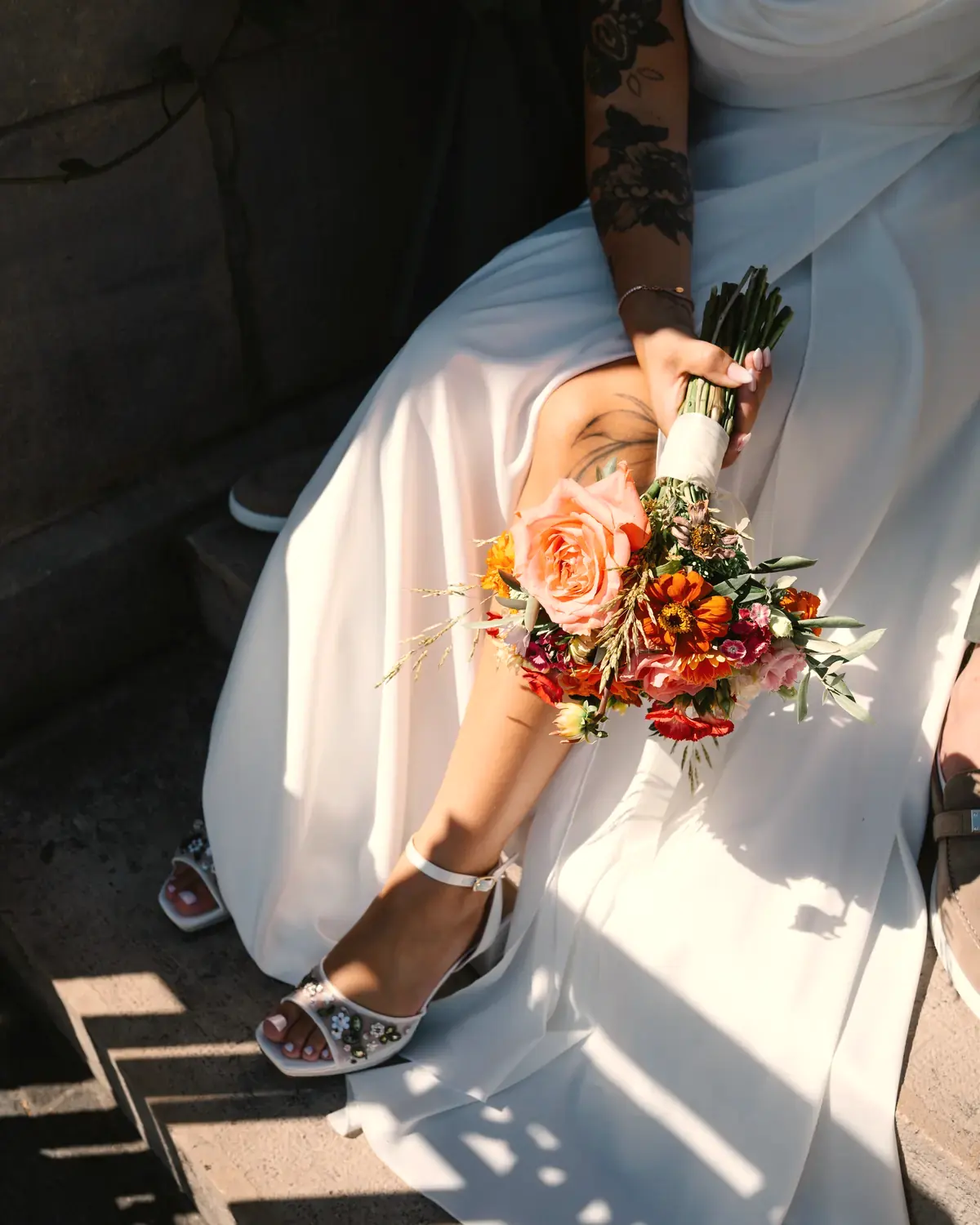 La mariée assise sur des marches, son bouquet coloré posé sur sa robe