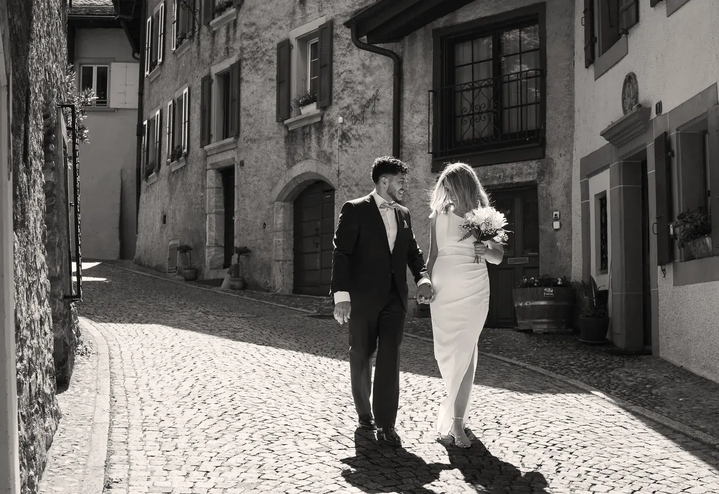 Un couple marche main dans la main dans une ruelle pavée, en noir et blanc